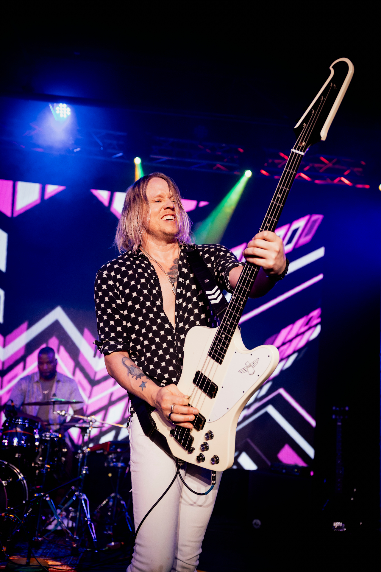 Bryce playing white Firebird bass under blue and pink stage lights